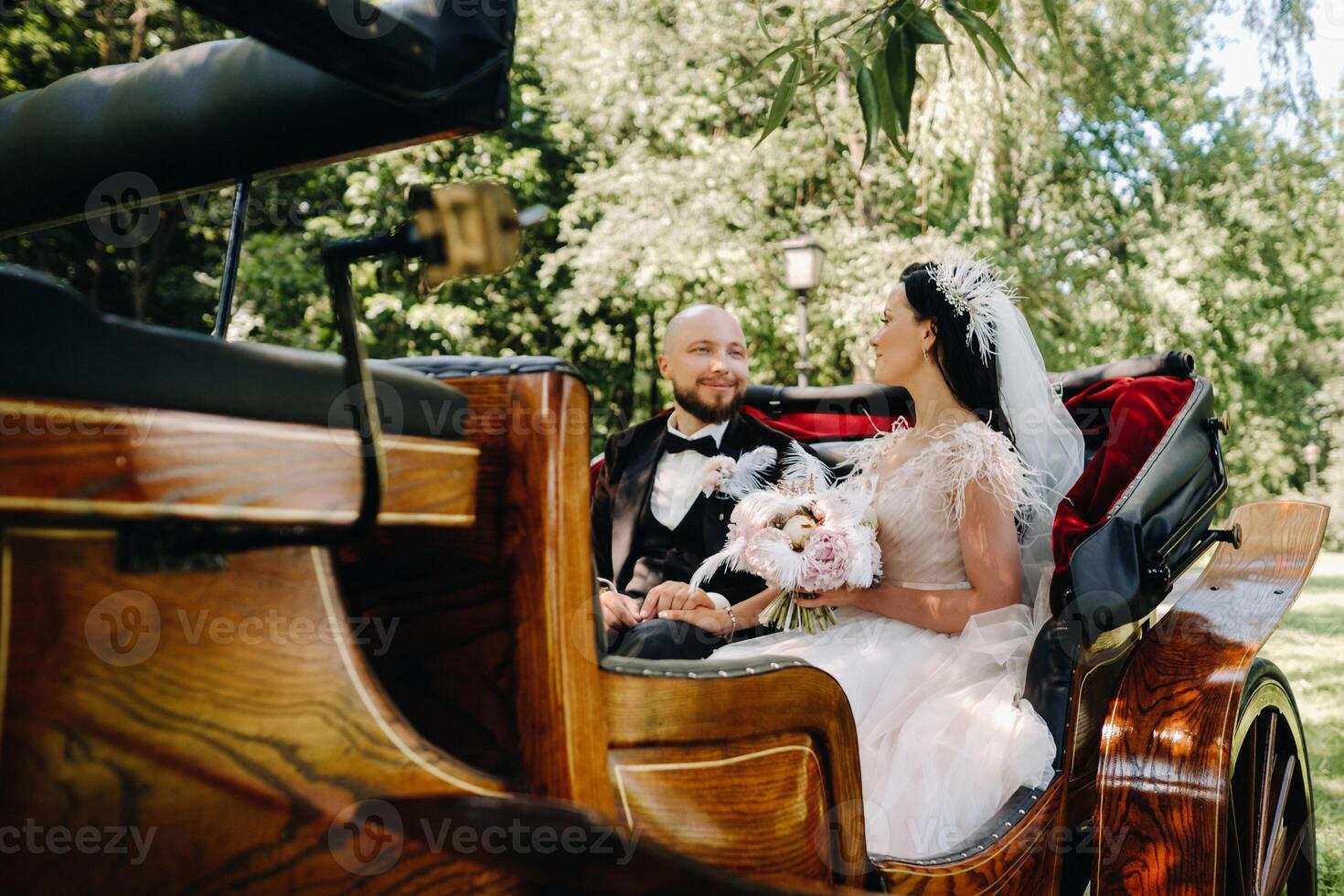 The bride and groom with a bouquet are sitting in a carriage in nature in retro style photo