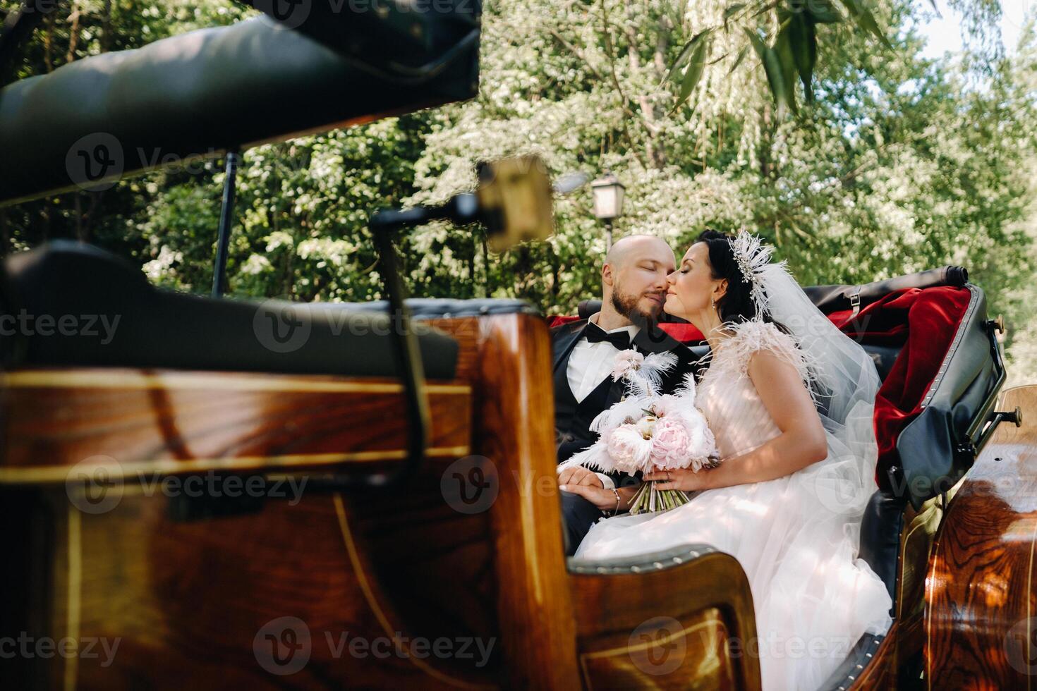 The bride and groom with a bouquet are sitting in a carriage in nature in retro style photo