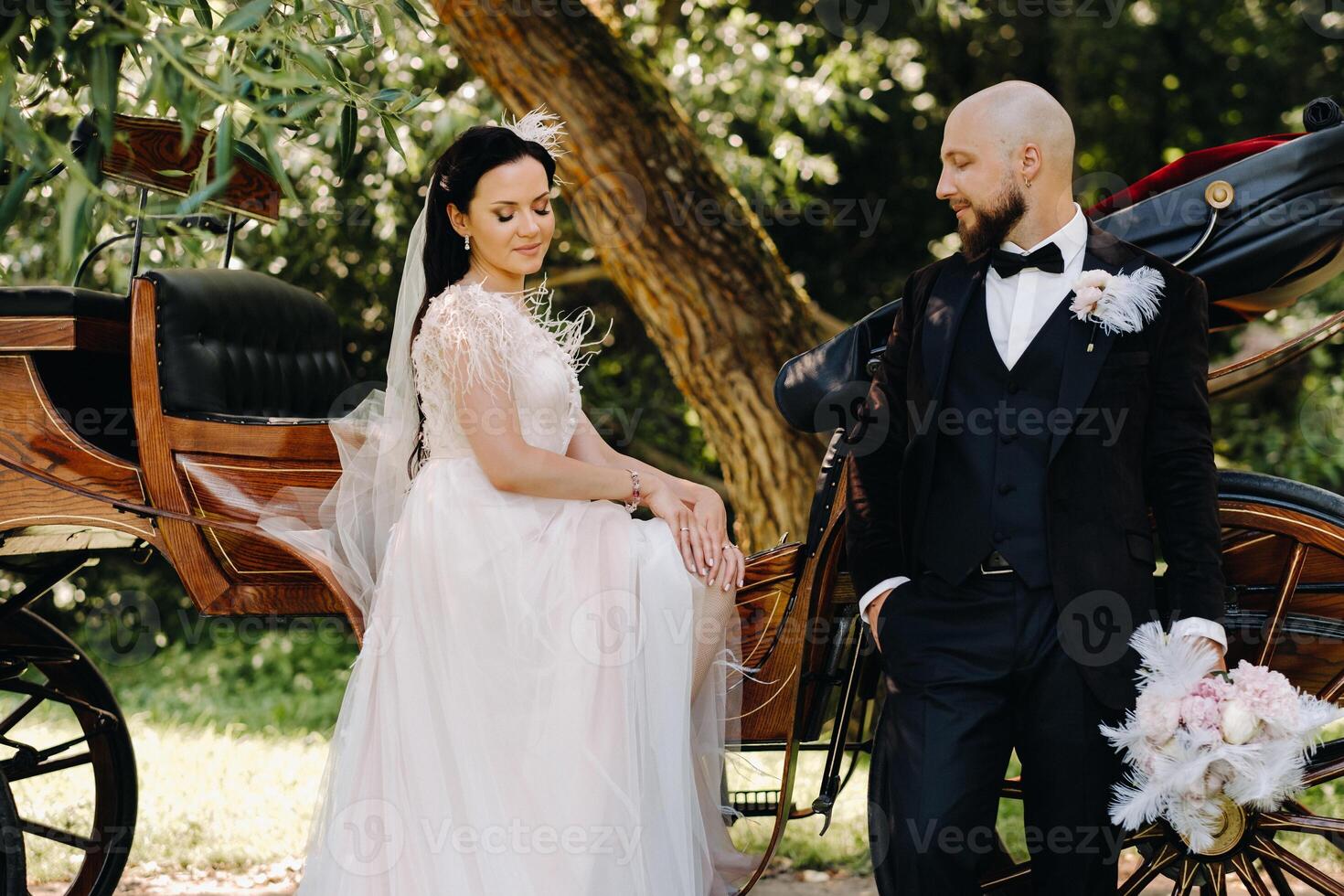 A couple of the bride and groom are standing near the carriage in nature in retro style photo