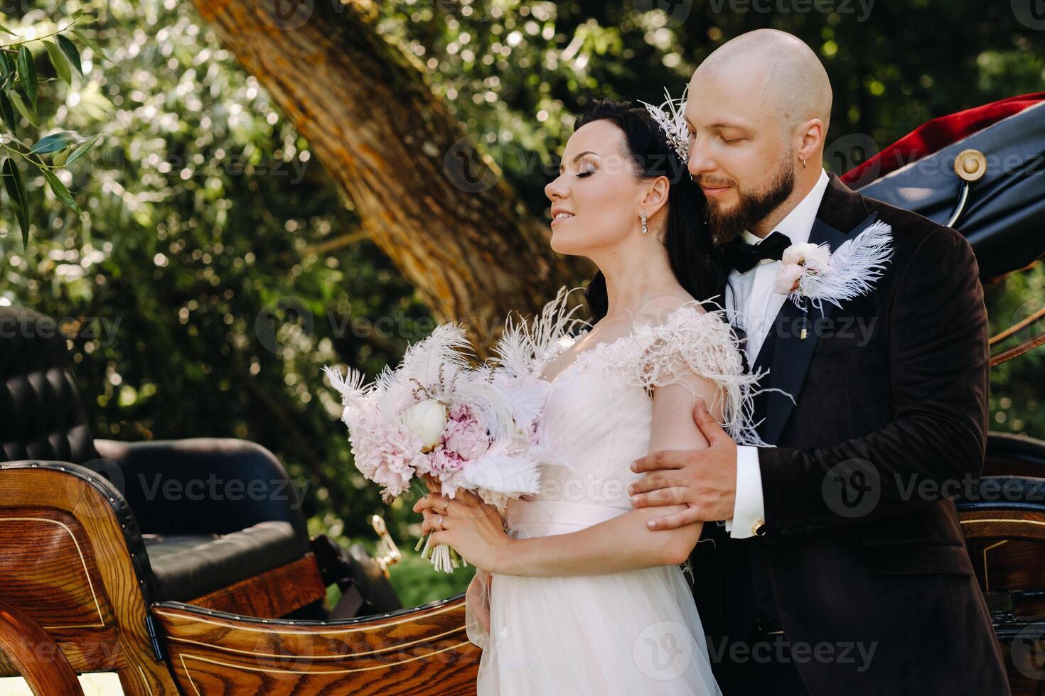A couple of the bride and groom are standing near the carriage in nature in retro style photo