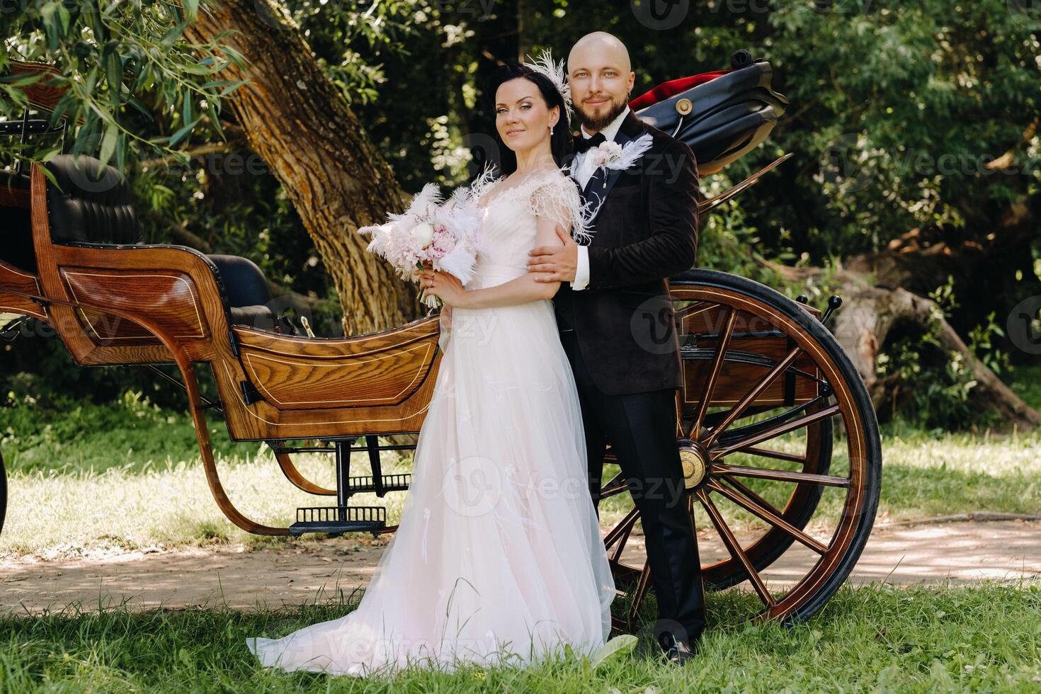 A couple of the bride and groom are standing near the carriage in nature in retro style photo