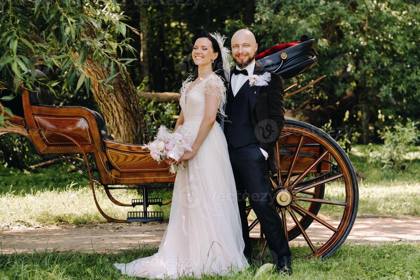 A couple of the bride and groom are standing near the carriage in nature in retro style photo