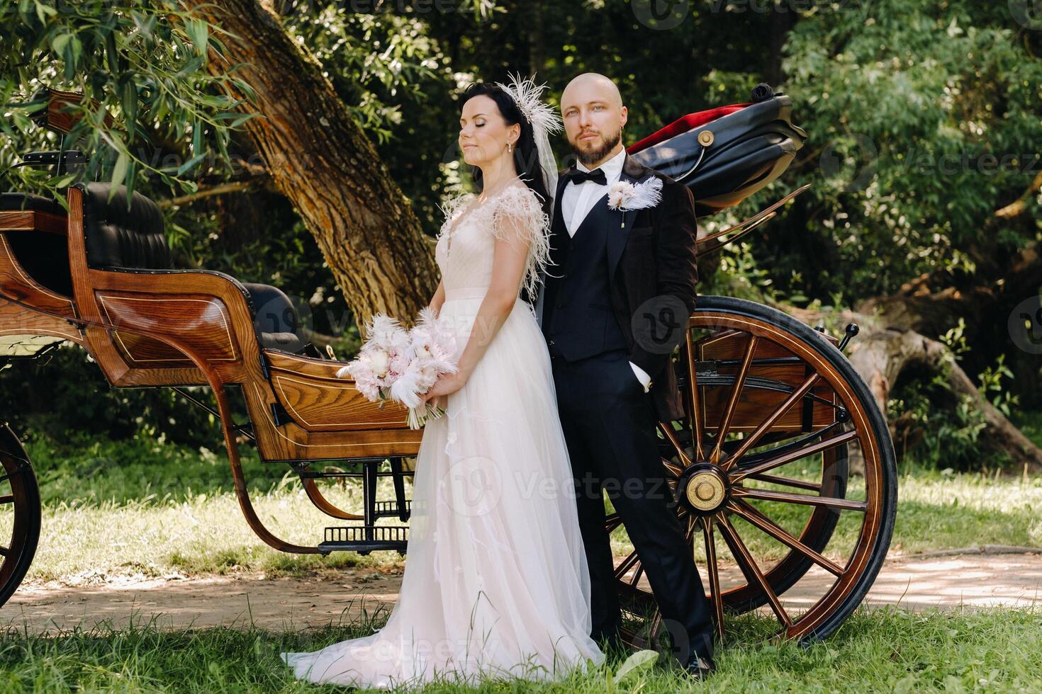 A couple of the bride and groom are standing near the carriage in nature in retro style photo