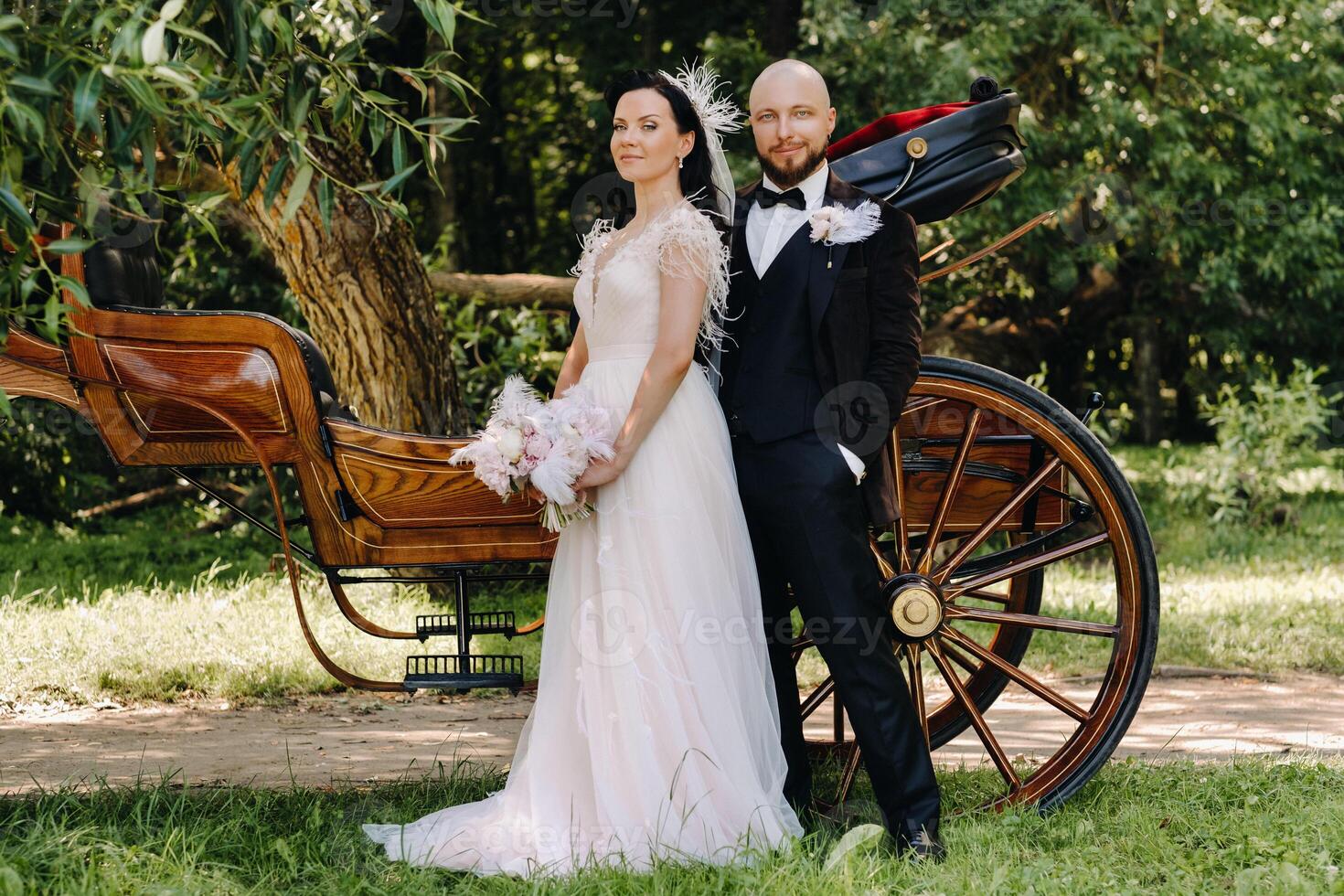 A couple of the bride and groom are standing near the carriage in nature in retro style photo