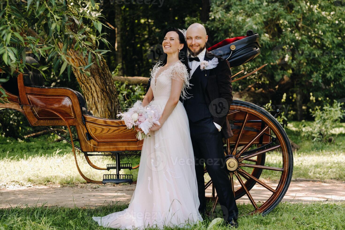 A couple of the bride and groom are standing near the carriage in nature in retro style photo