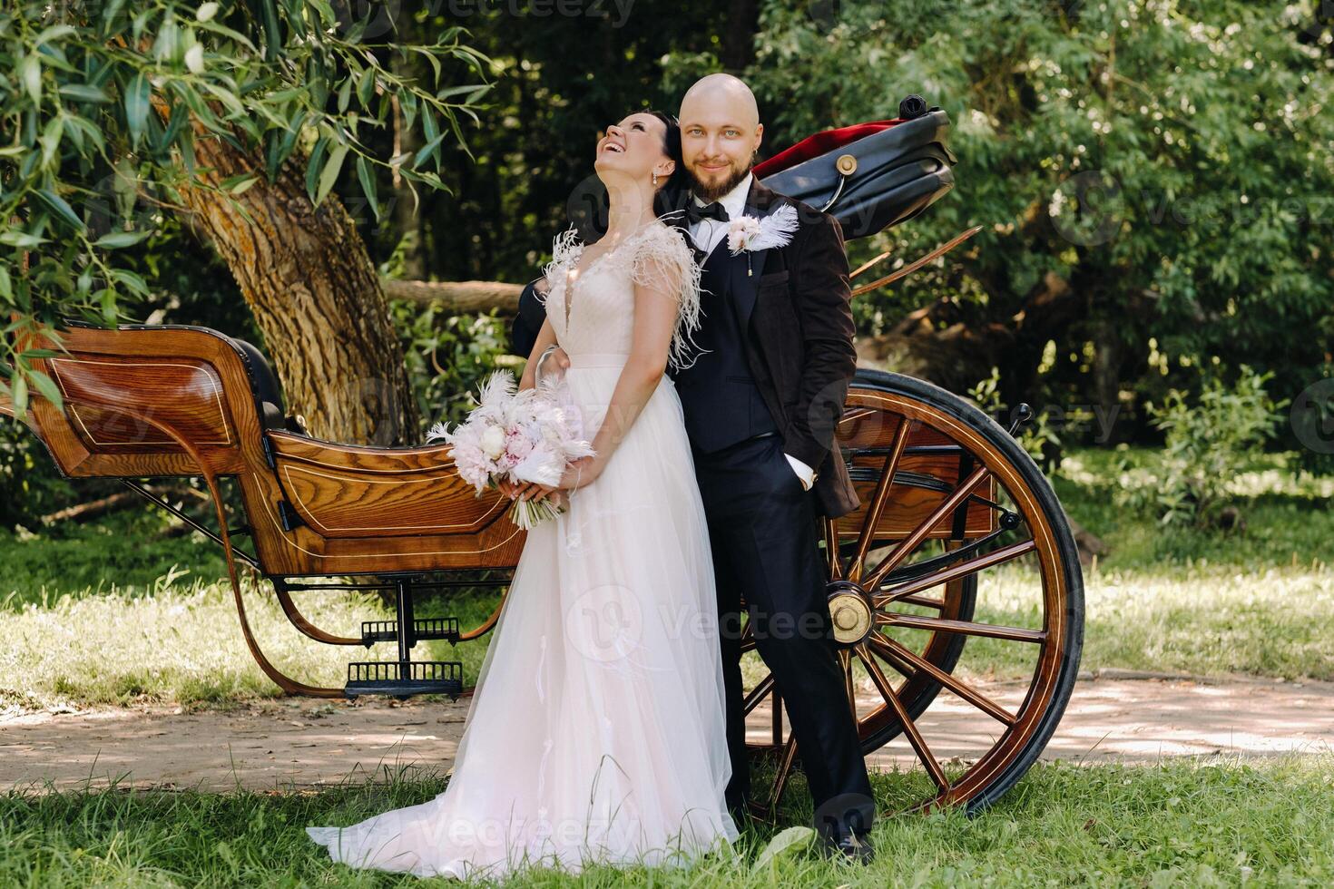 A couple of the bride and groom are standing near the carriage in nature in retro style photo
