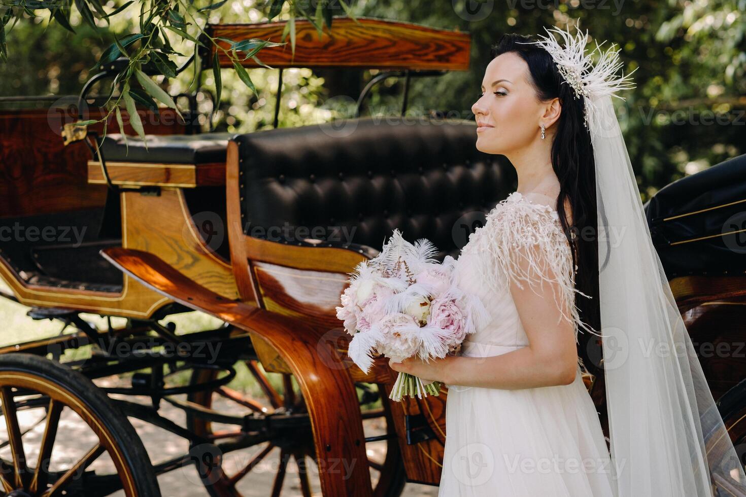 A stylish bride with a bouquet stands near a carriage in nature in retro style photo