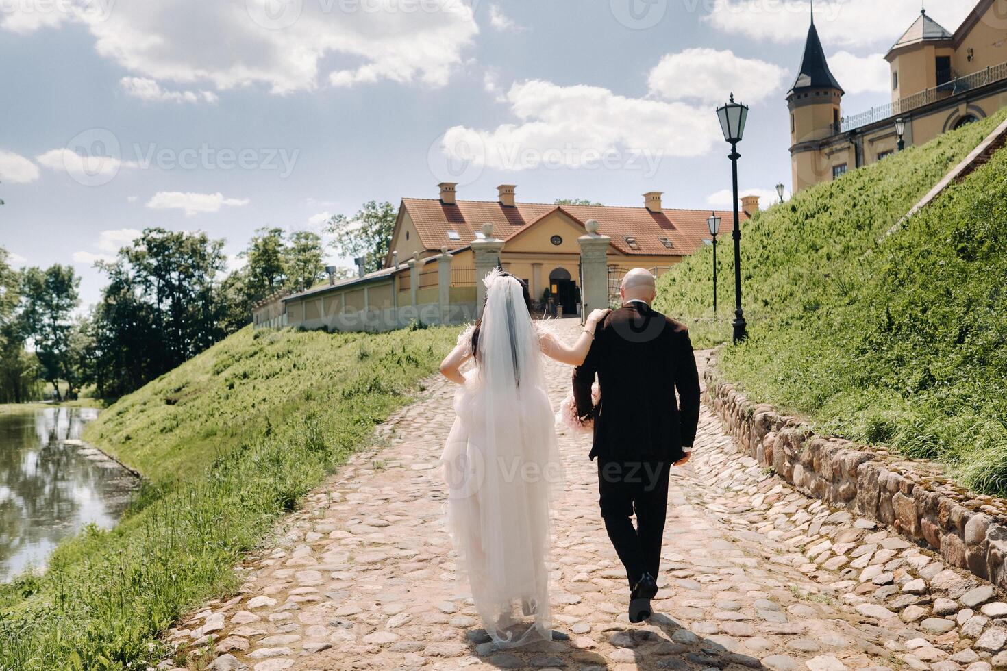 rear view. the bride and groom walk along the stone road towards the castle photo