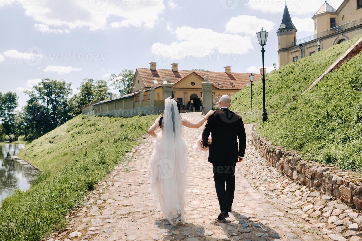 rear view. the bride and groom walk along the stone road towards the castle photo