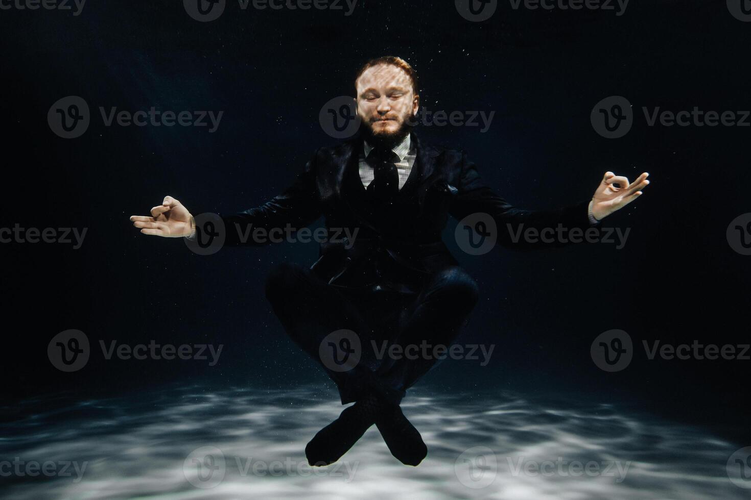 A man in a strict suit under water in the Lotus position photo