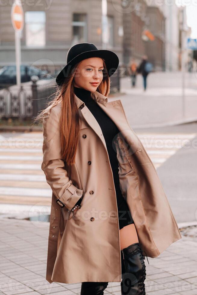 Stylish young woman in a beige coat in a black hat on a city street. Women's street fashion. Autumn clothing.Urban style photo