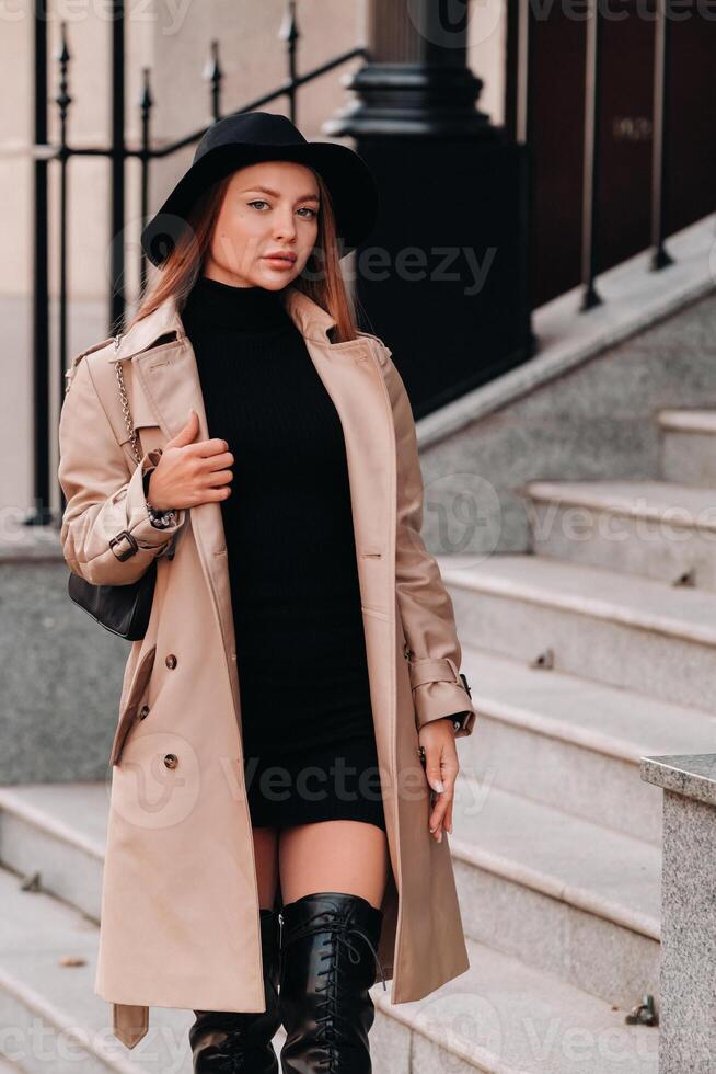 Stylish young woman in a beige coat in a black hat on a city street. Women's street fashion. Autumn clothing.Urban style photo