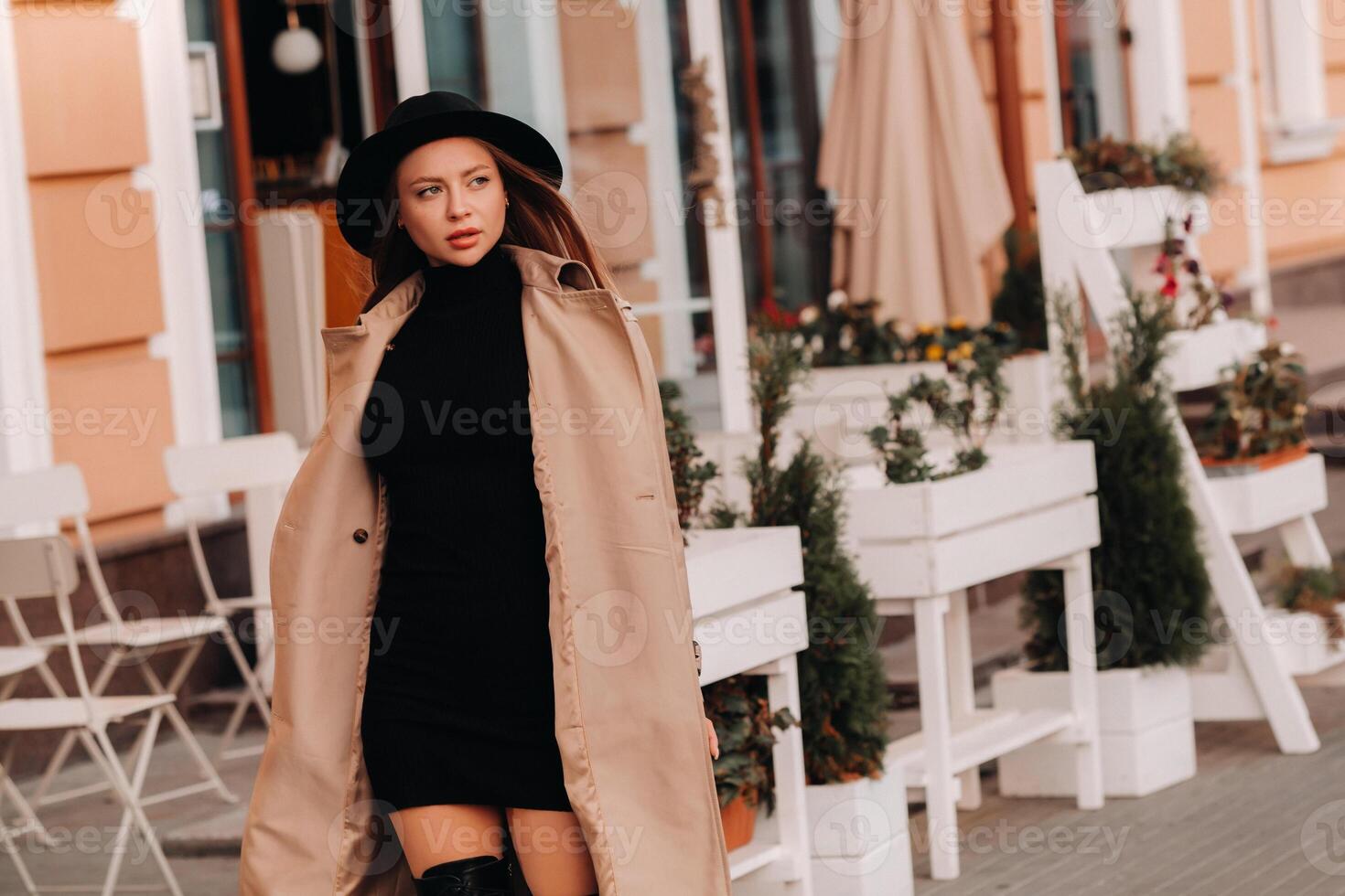 Stylish young woman in a beige coat in a black hat on a city street. Women's street fashion. Autumn clothing.Urban style photo