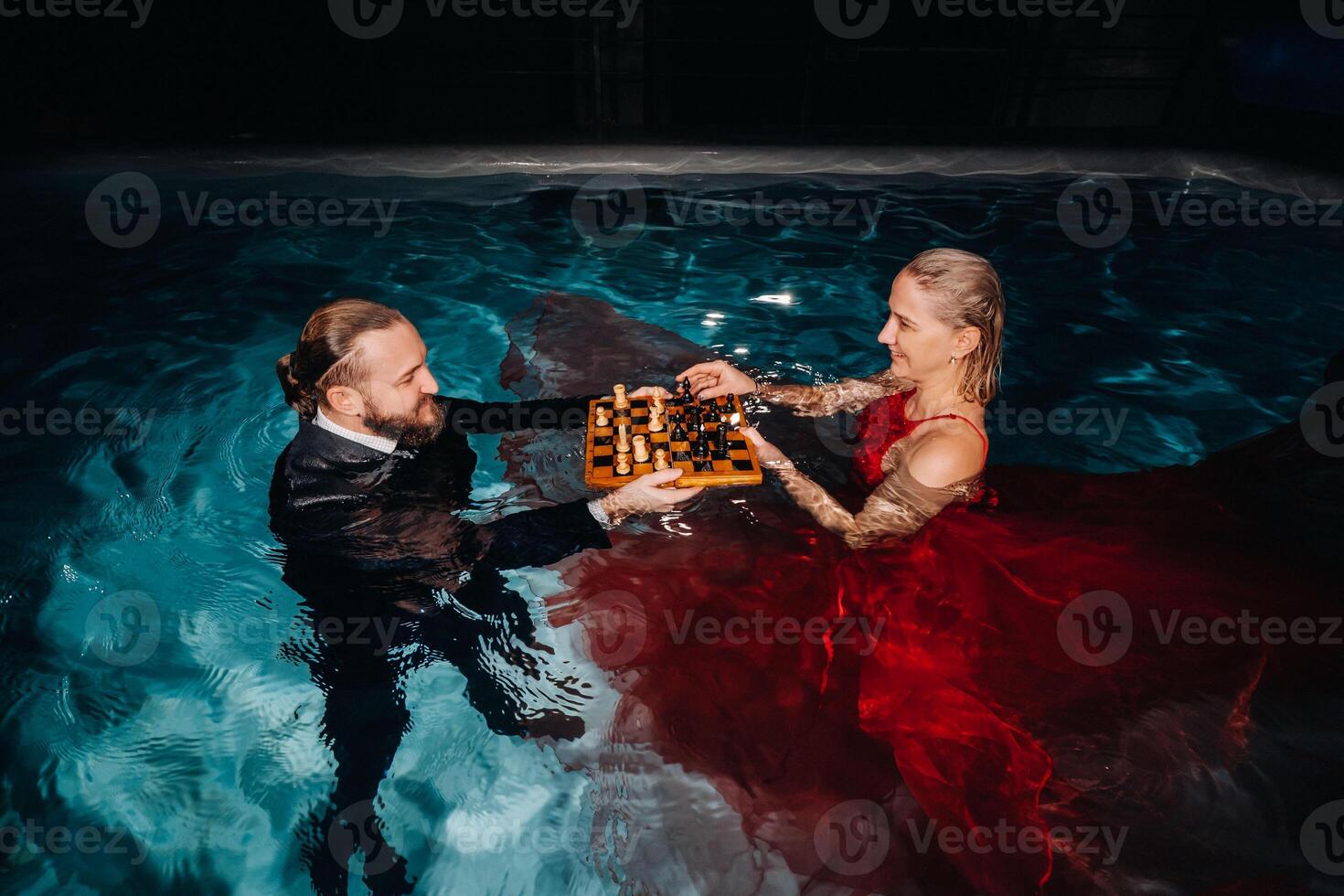 a man in a suit and a girl in a red dress play chess on the water in the pool photo