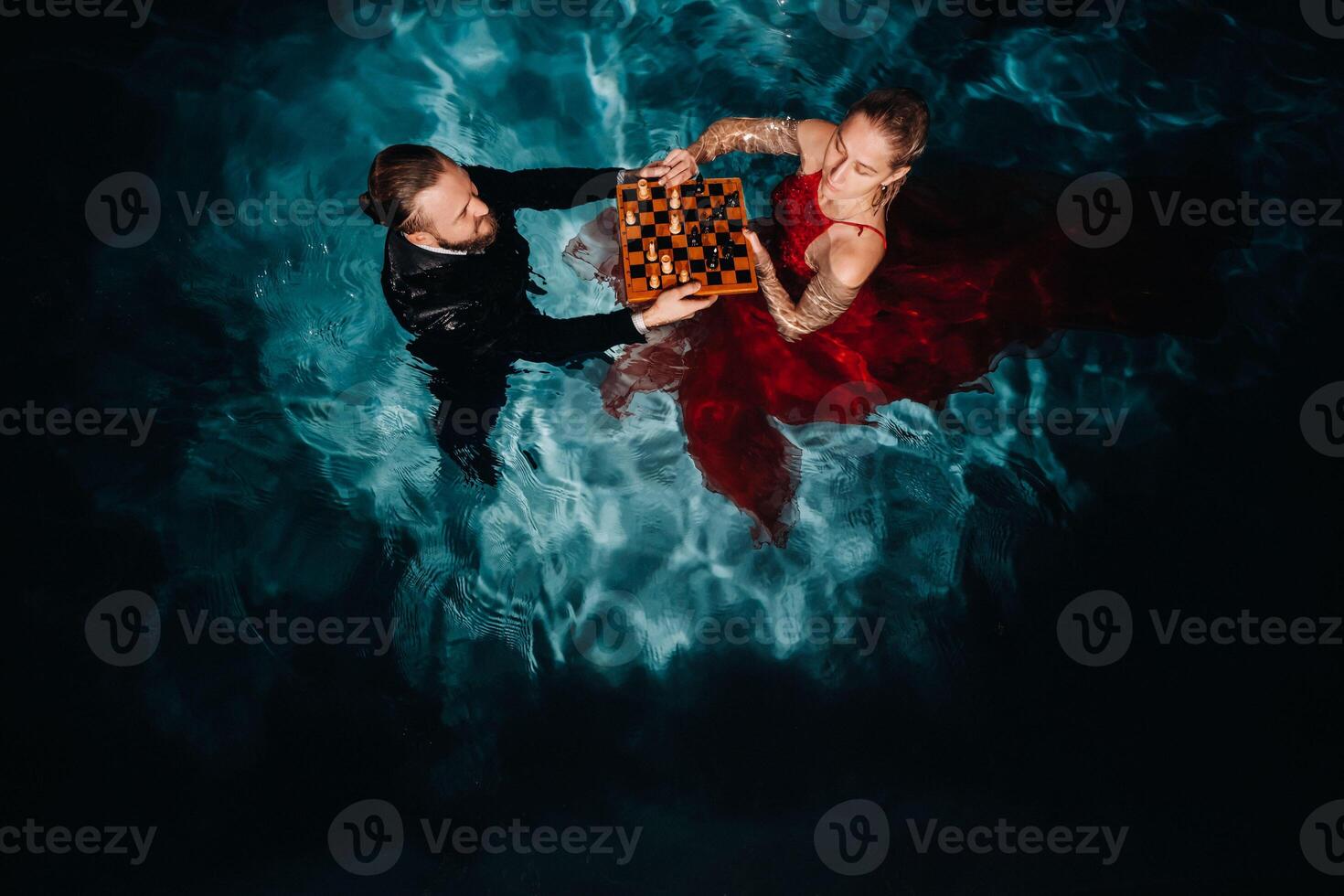 a man in a suit and a girl in a red dress play chess on the water in the pool photo