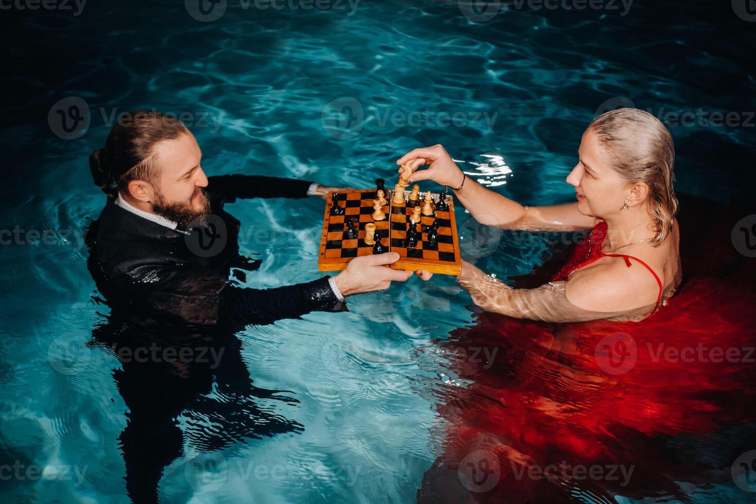 a man in a suit and a girl in a red dress play chess on the water in the pool photo