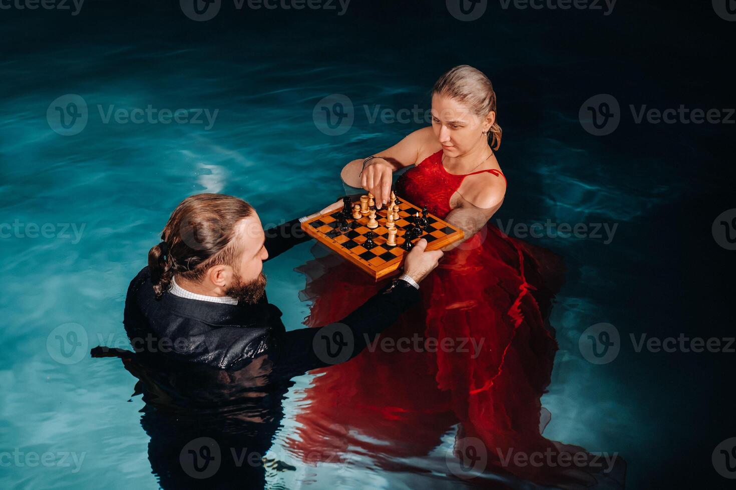 a man in a suit and a girl in a red dress play chess on the water in the pool photo