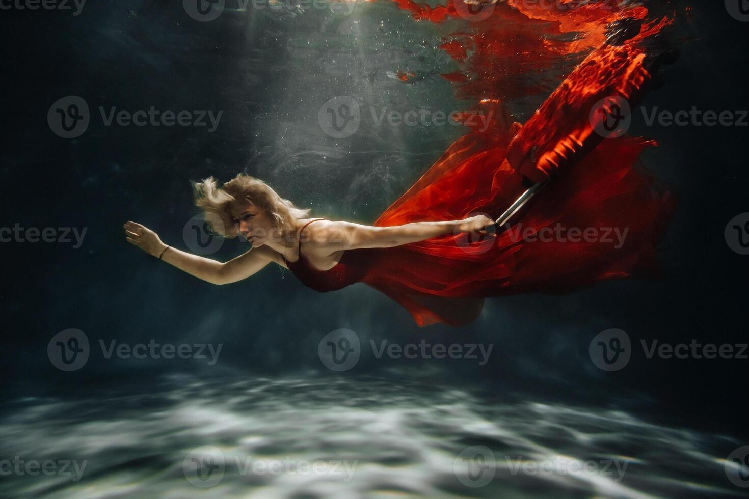 A girl in a red dress is floating under the water with a suitcase.Journey under the water of a single woman.The concept of underwater tourism photo