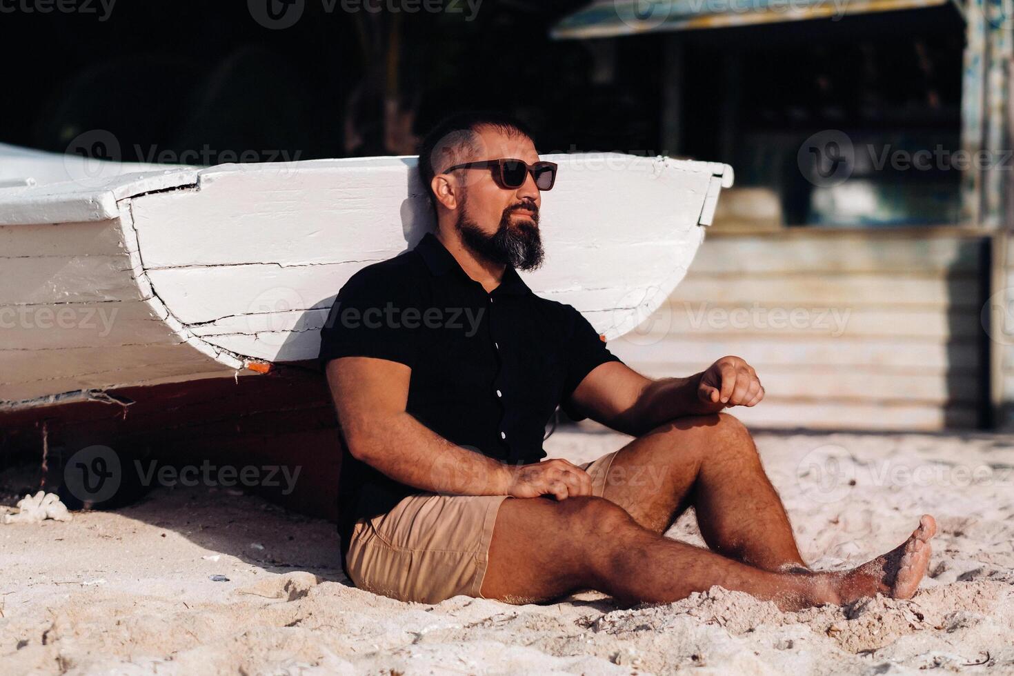 Portrait of a beautiful brutal man, enjoying and relaxing, sitting on the beach of the island of Mauritius.The man on the beach of Le Morne in the black clothes and glasses. tropical beach photo