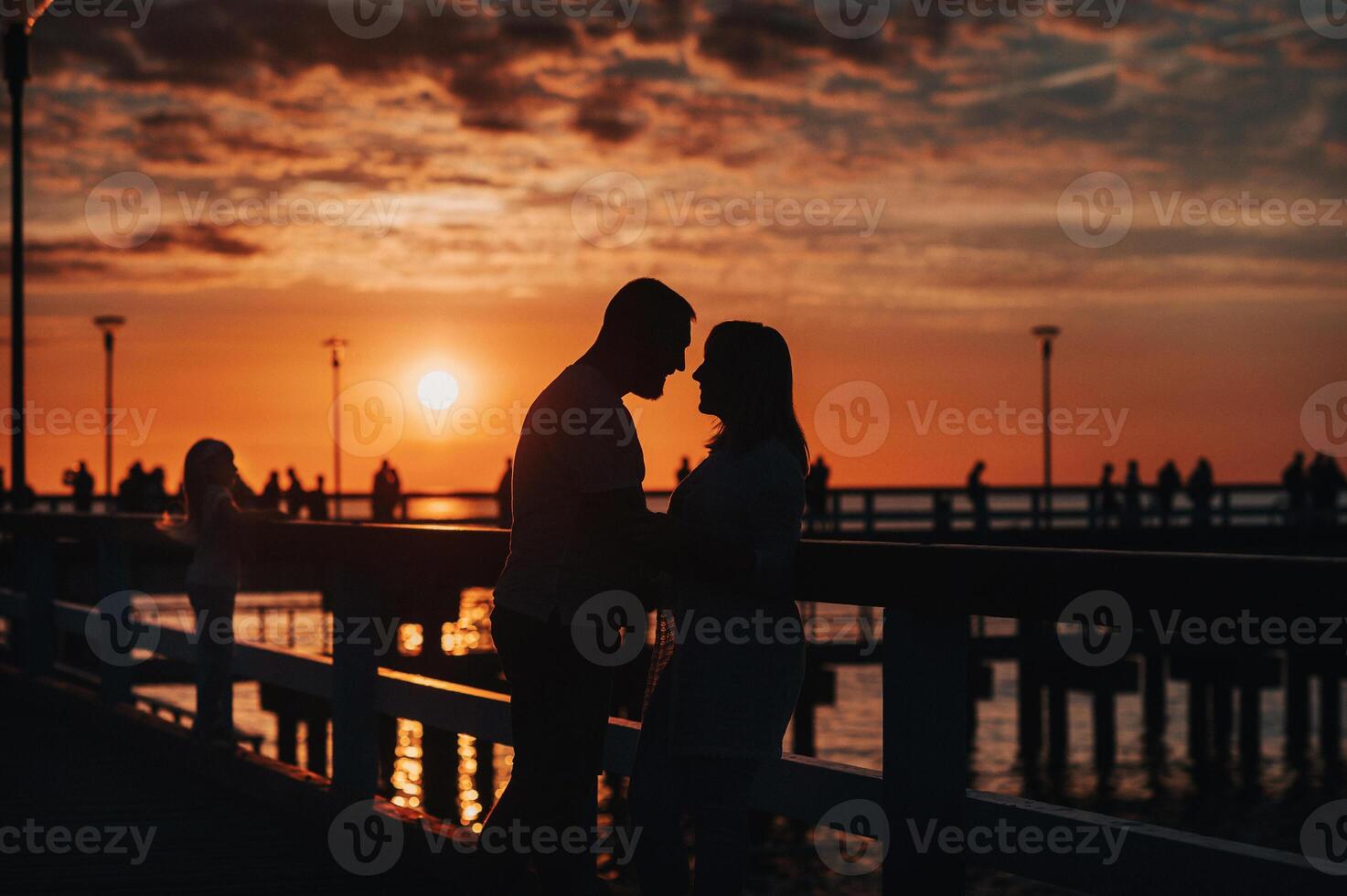 Portrait silhouette of a beautiful newlywed couple. A loving man hugs a girl at sunset, against the background of the sea standing on the pier. photo