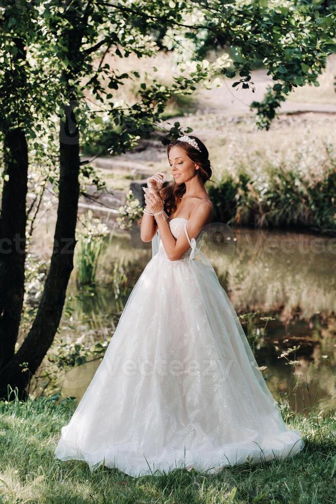 An elegant bride in a white dress, gloves with a bouquet on a waterfall in the Park, enjoying nature.Model in a wedding dress and gloves in the forest.Belarus photo