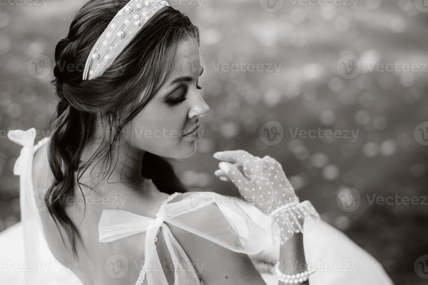 An elegant bride in a white dress, gloves and bare feet is sitting near a waterfall in the Park enjoying nature.A model in a wedding dress and gloves at a nature Park.Belarus. black and white photo