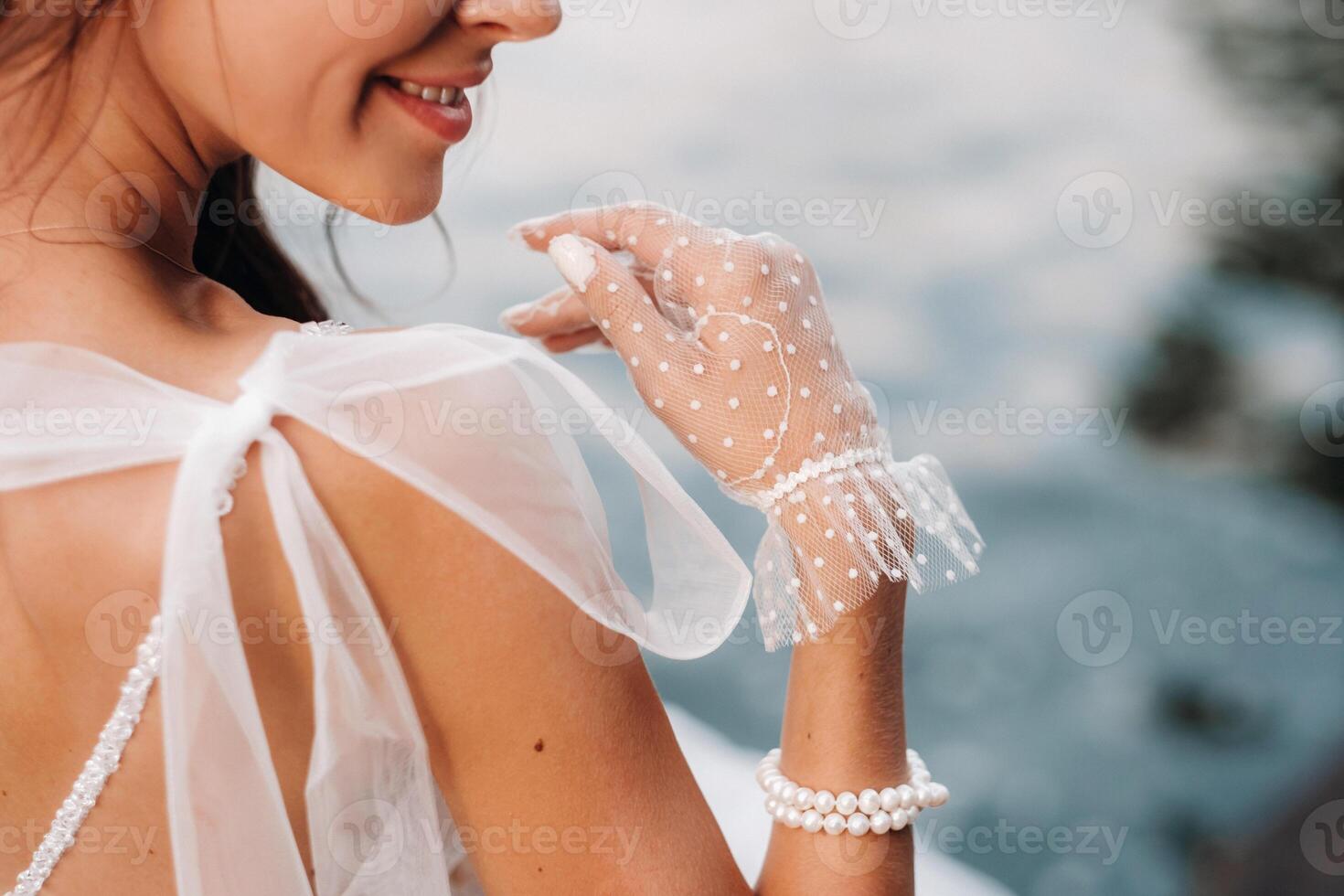 An elegant bride in a white dress, gloves and bare feet is sitting near a waterfall in the Park enjoying nature.A model in a wedding dress and gloves at a nature Park.Belarus photo