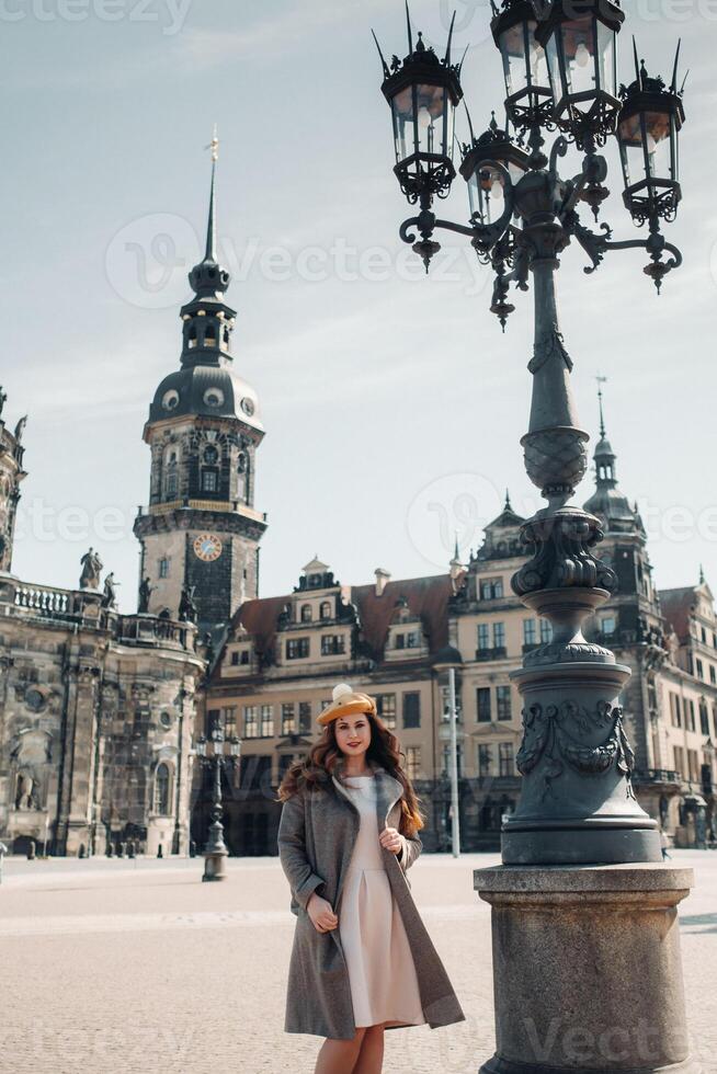 stylish young beautiful girl in a coat and hat near a lamp in the old city of Dresden.Germany.Walking around the city in Germany photo