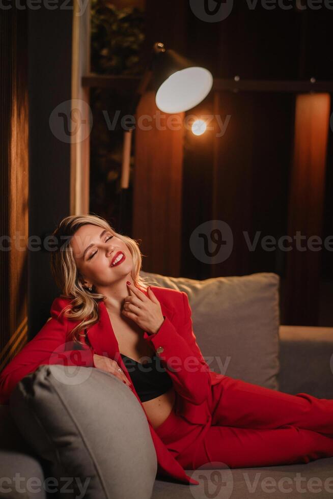 a beautiful girl dressed in a red formal suit posing in a modern interior photo