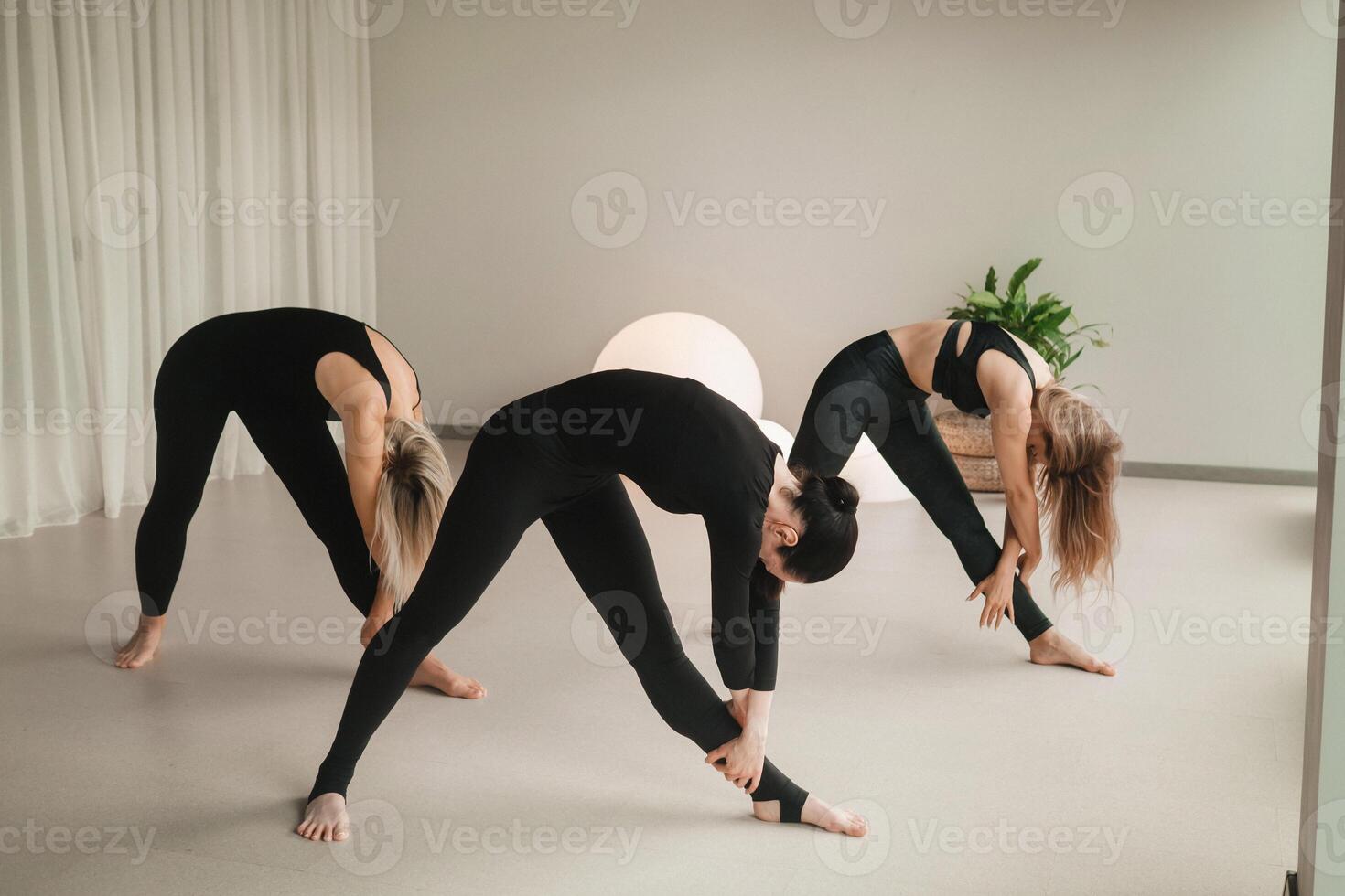 A group of girls in black doing yoga poses indoors. Women are engaged in fitness photo