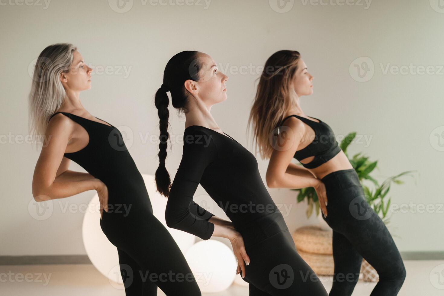A group of girls in black doing yoga poses indoors. Women are engaged in fitness photo