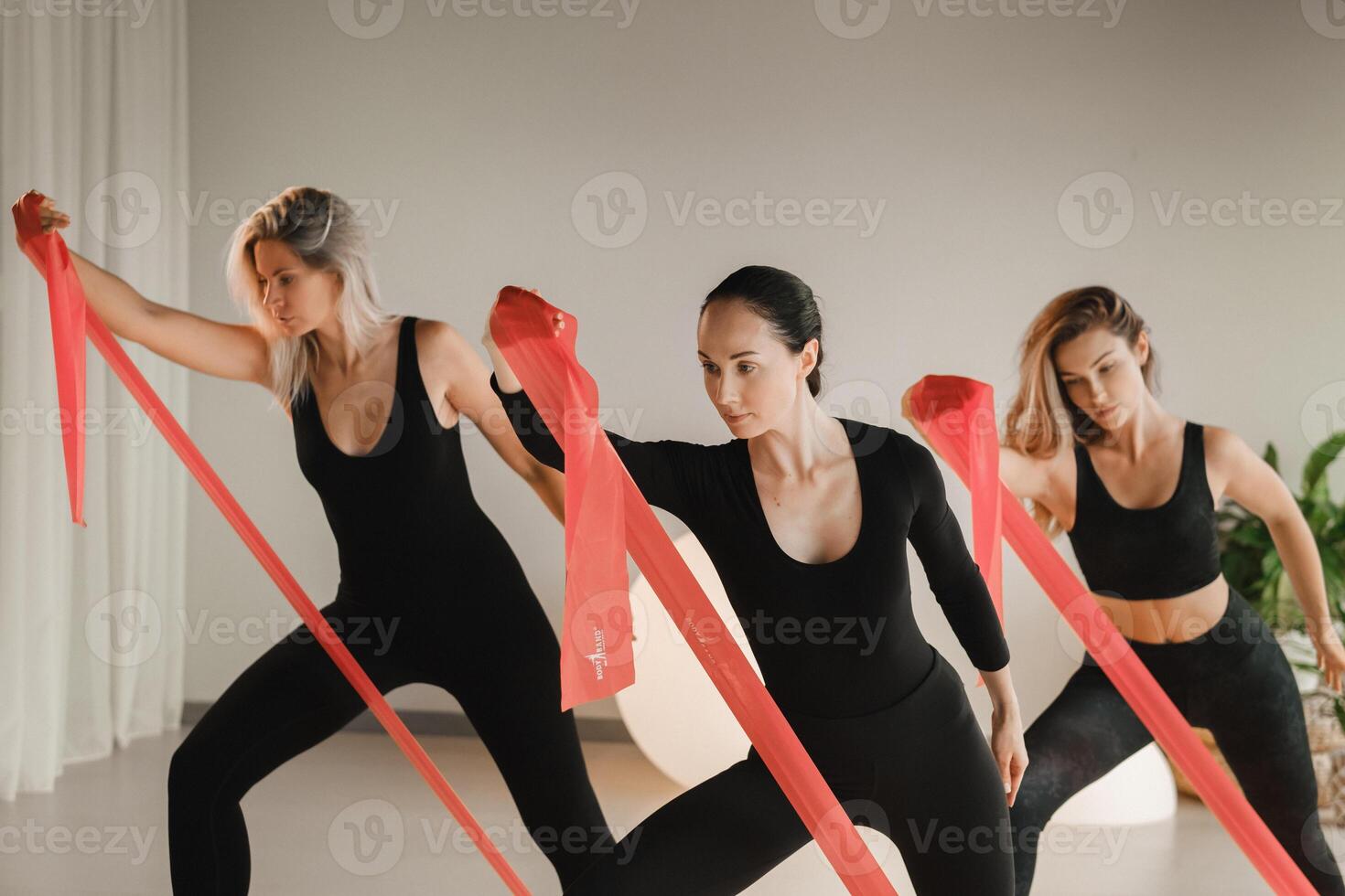 Girls in black are doing fitness with red ribbons indoors photo