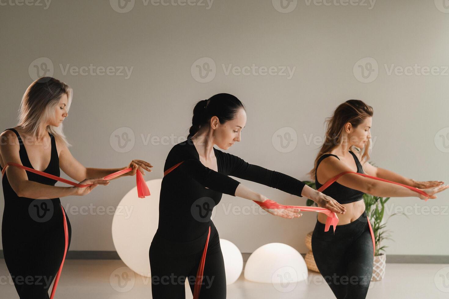Girls in black are doing fitness with red ribbons indoors photo
