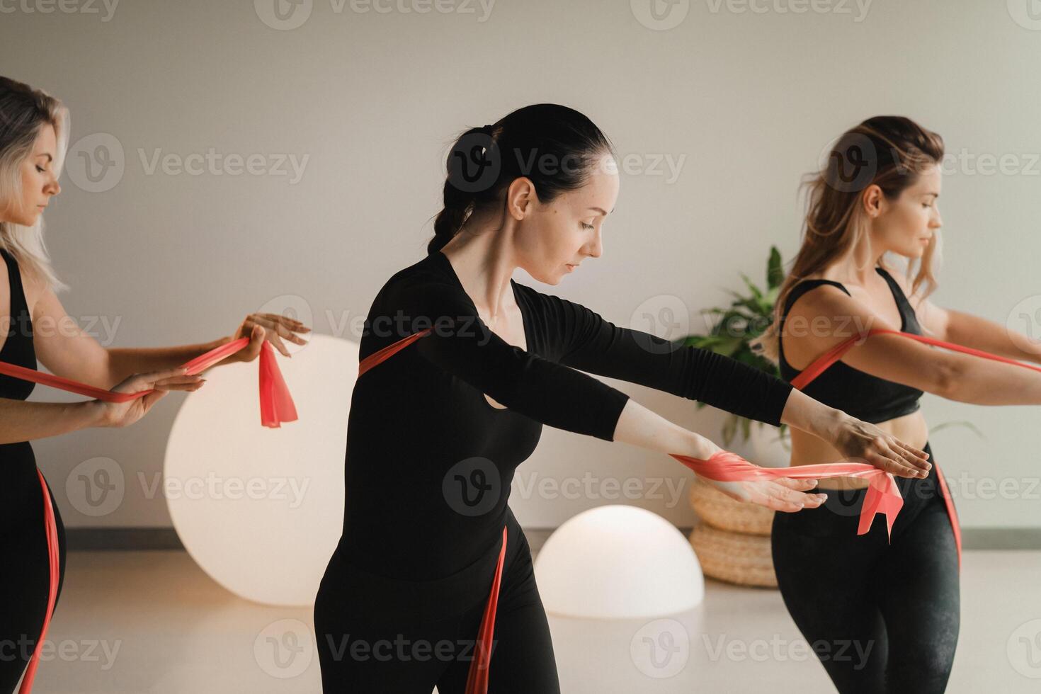 Girls in black are doing fitness with red ribbons indoors photo