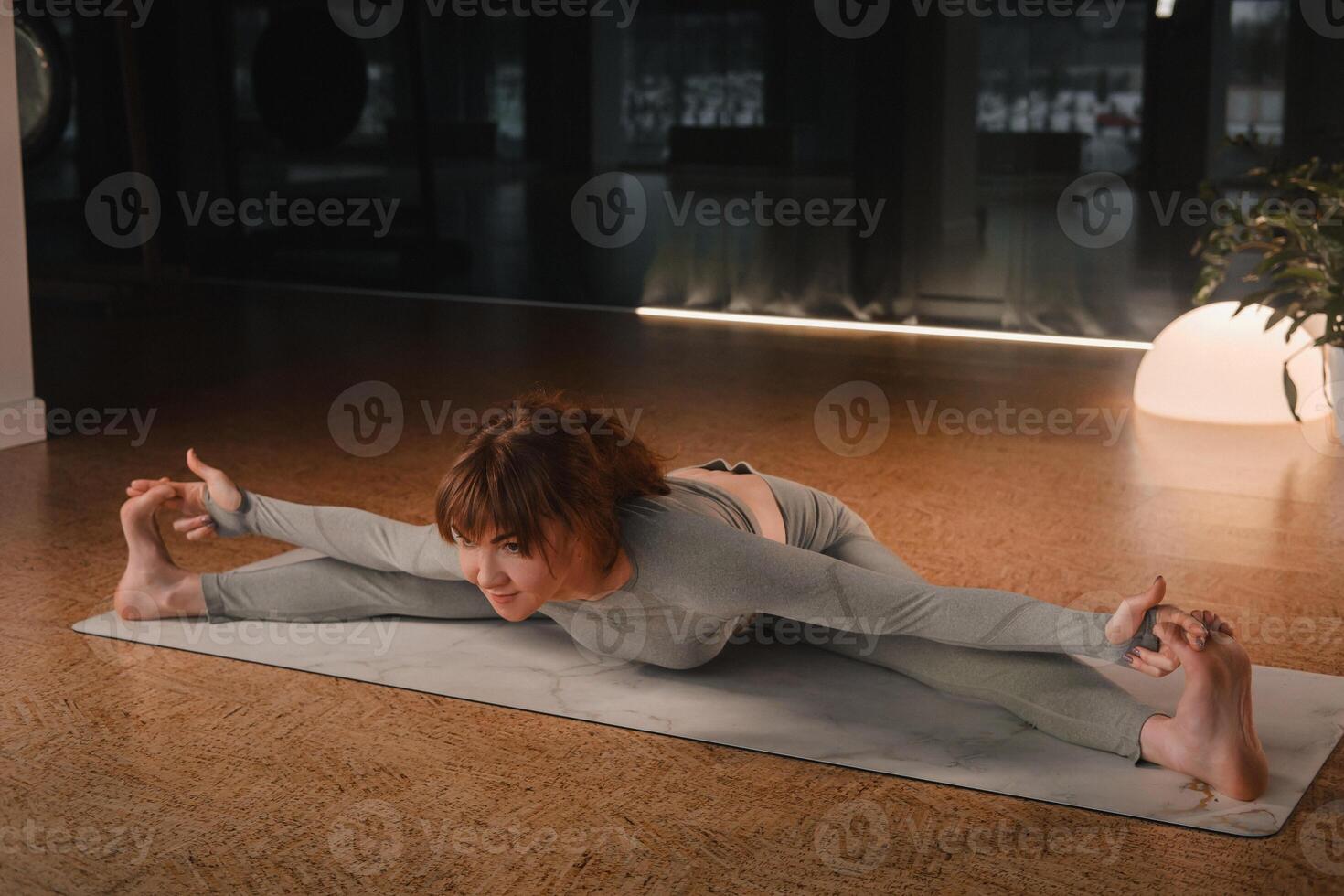 A girl in a gray sports uniform does yoga on a mat in the gym photo