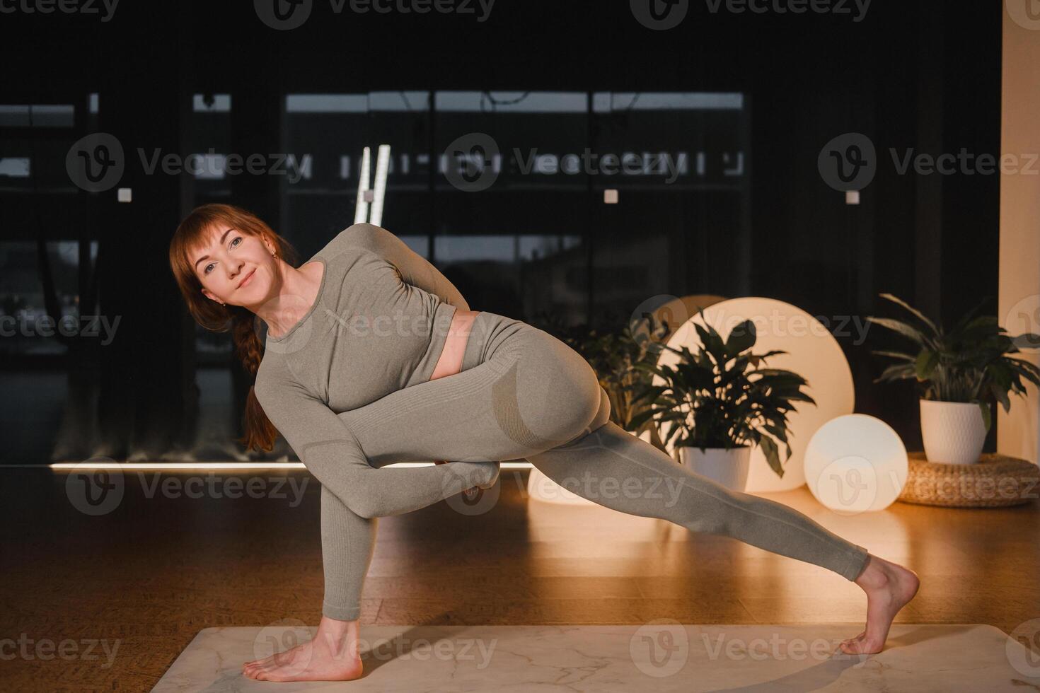 A girl in a gray sports uniform does yoga on a mat in the gym photo