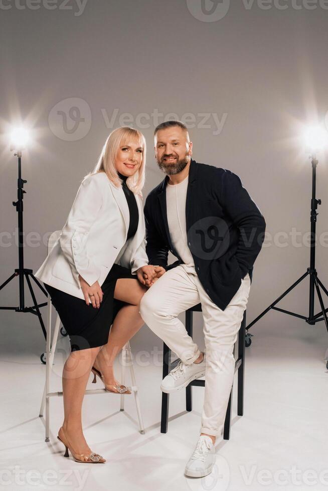 A man and a woman in strict clothes pose against the background in the studio photo