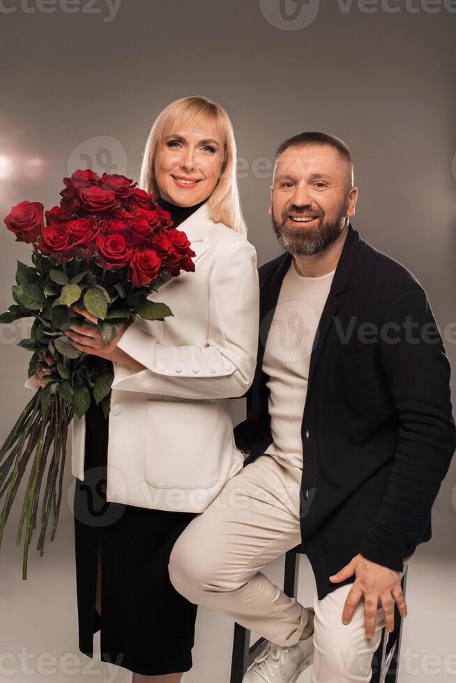A man and a woman with flowers in their hands in strict clothes pose in the background in the studio photo
