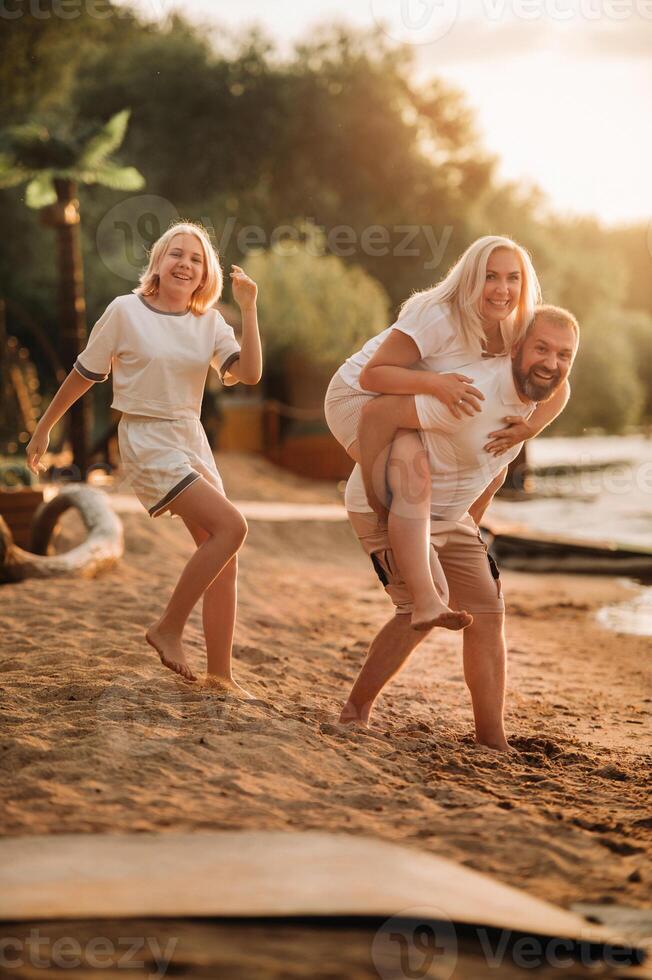 Happy family - father, mother and daughter in light clothes having fun together on the beach in summer photo