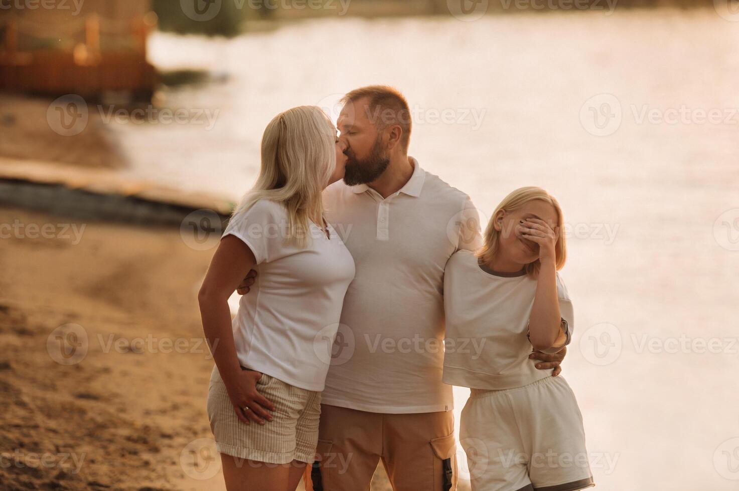 Happy family - father, mother and daughter in light clothes having fun together on the beach in summer photo