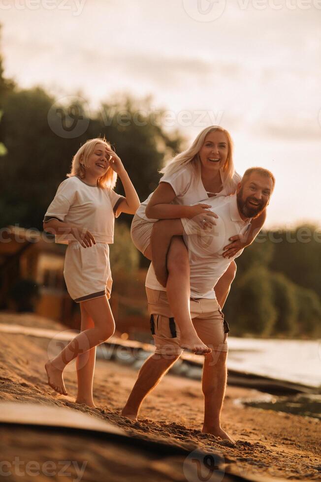 Happy family - father, mother and daughter in light clothes having fun together on the beach in summer photo