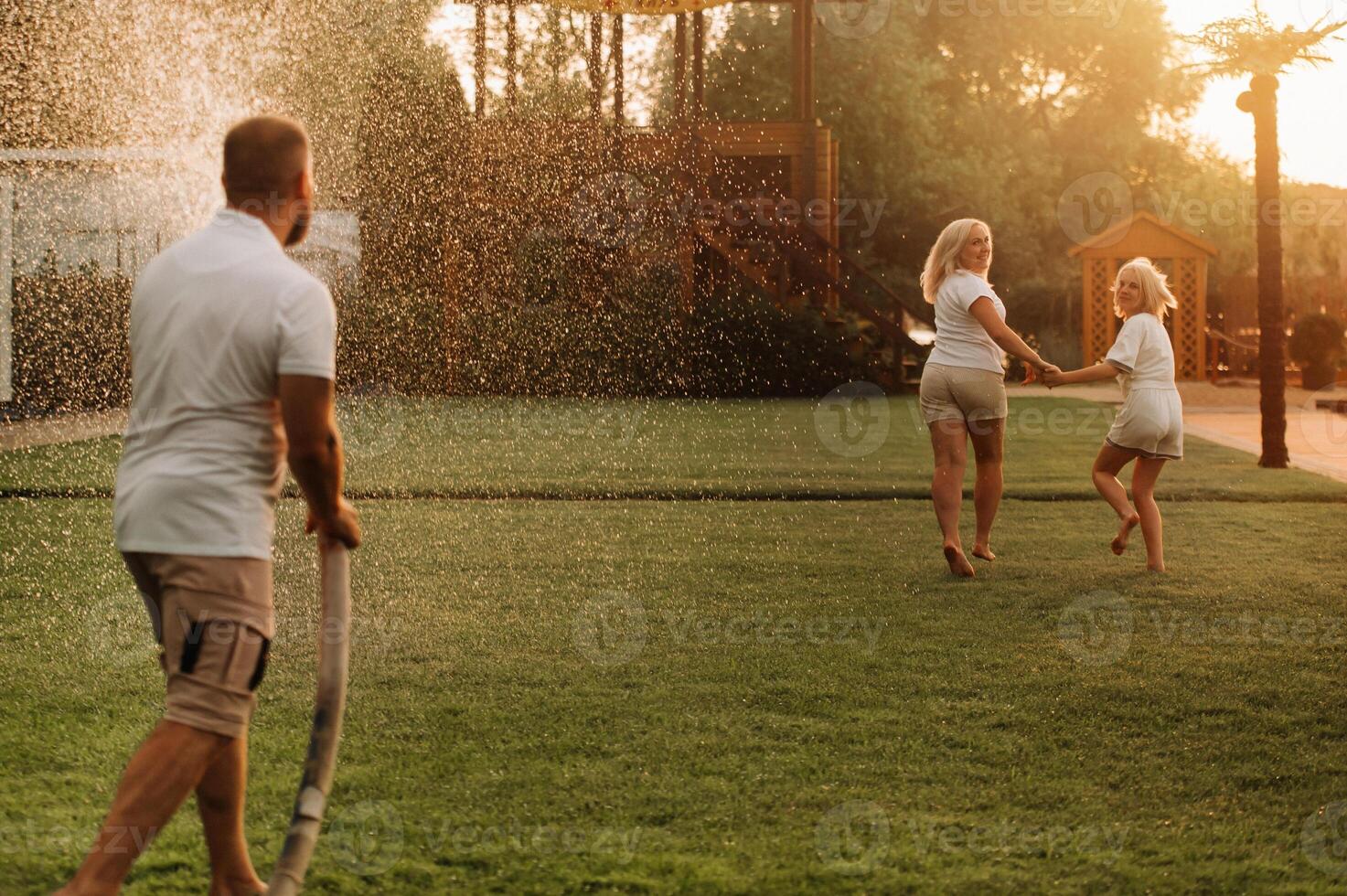 A man pours water from a hose on his wife and daughter on the lawn photo