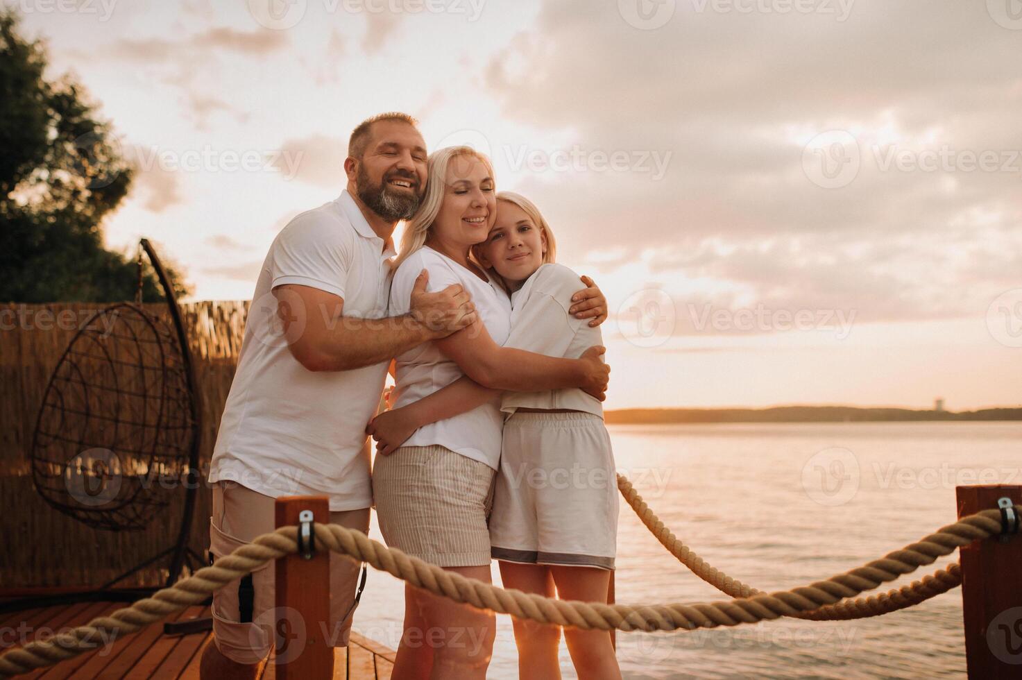 Happy family - father, mother and daughter in light clothes hugging together on the beach in summer photo