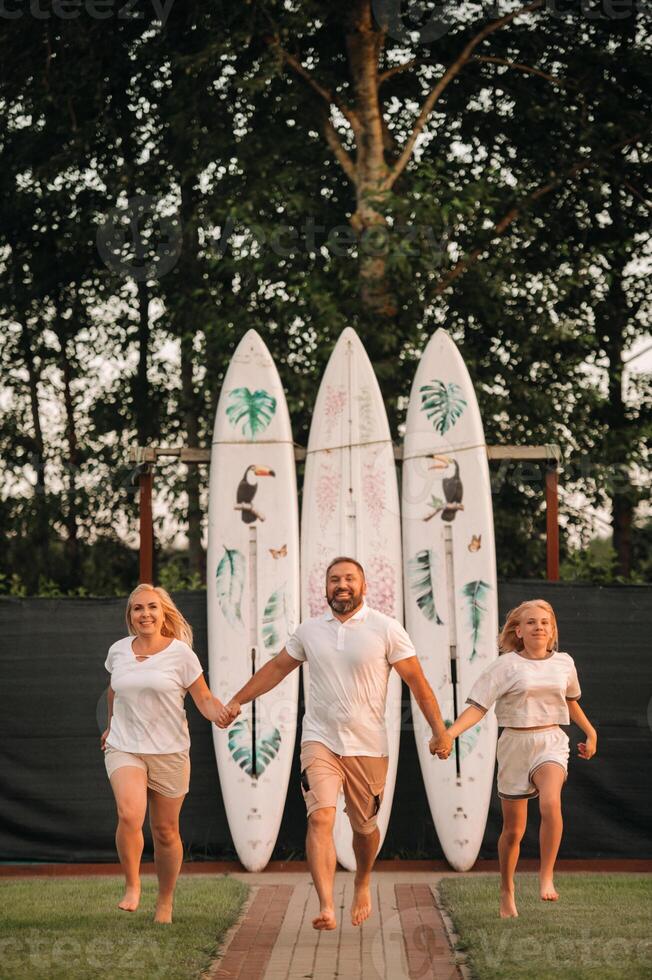A family of three stands against a backdrop of surfboards at sunset photo