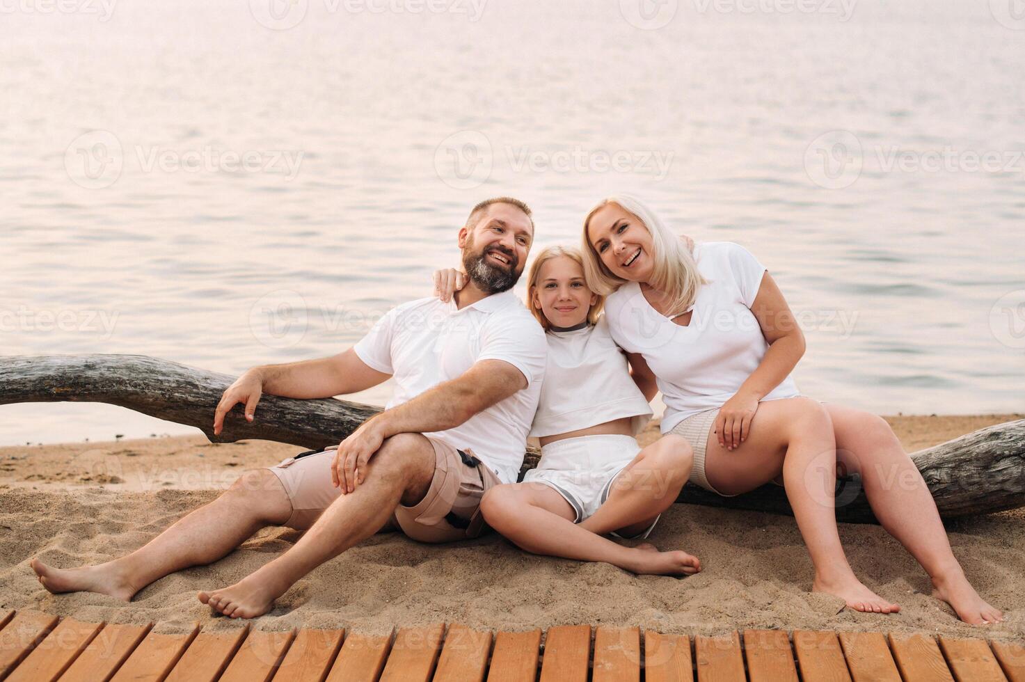 Happy family of three relaxing sitting on the beach after sunset photo