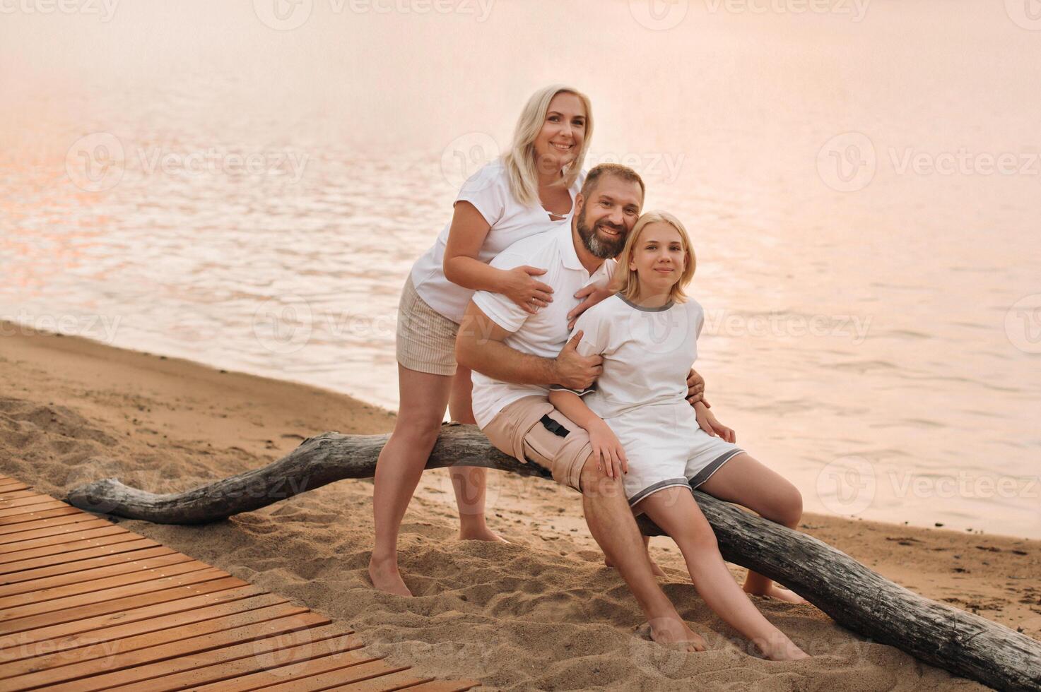 Happy family of three relaxing sitting on the beach after sunset photo