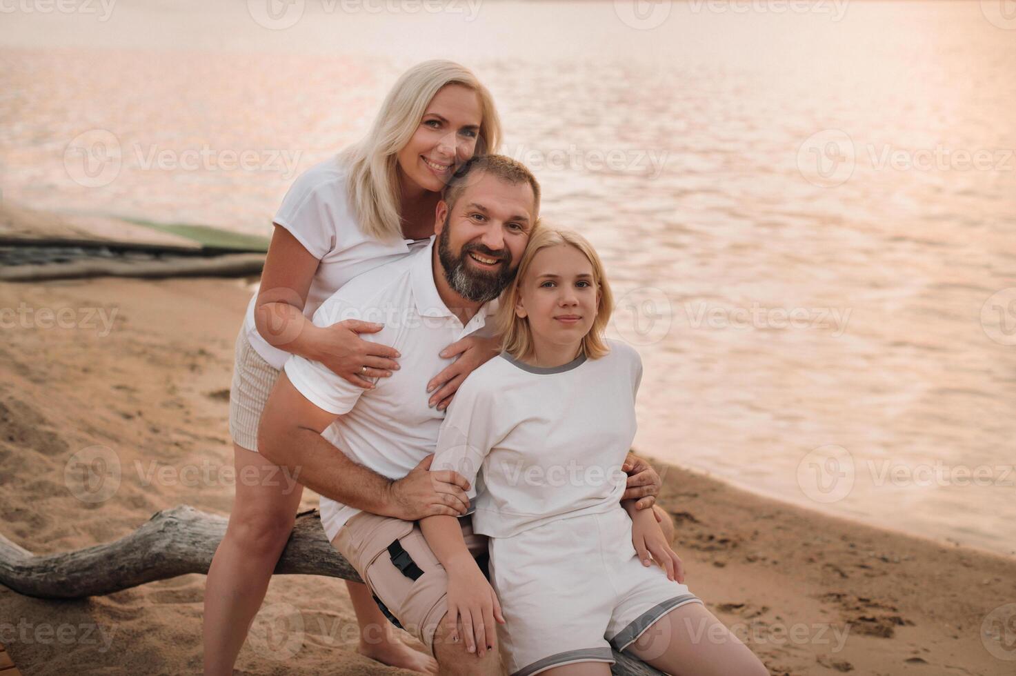 Happy family of three relaxing sitting on the beach after sunset photo