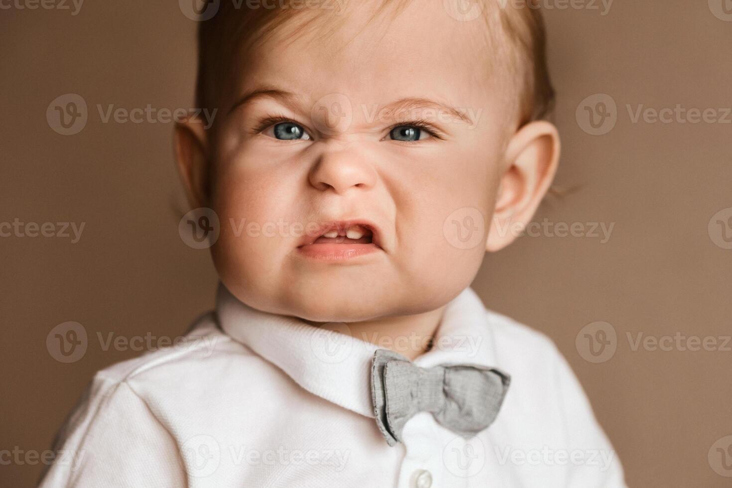Portrait of a little boy in a white shirt with a bow tie grimacing on camera photo