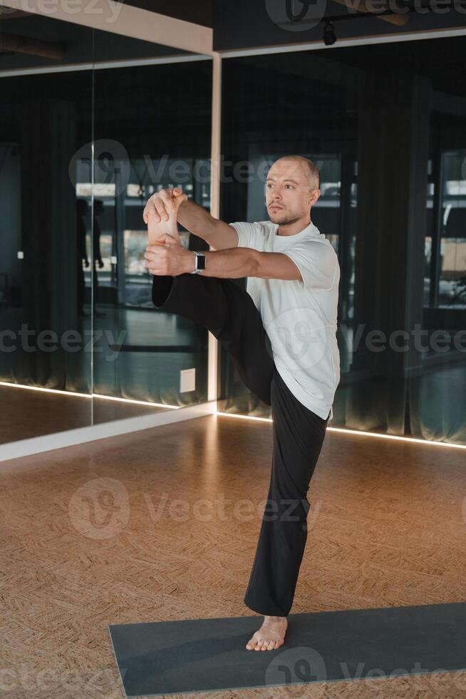 An athletic young man does exercises in the fitness room. A professional guy does yoga in the gym photo