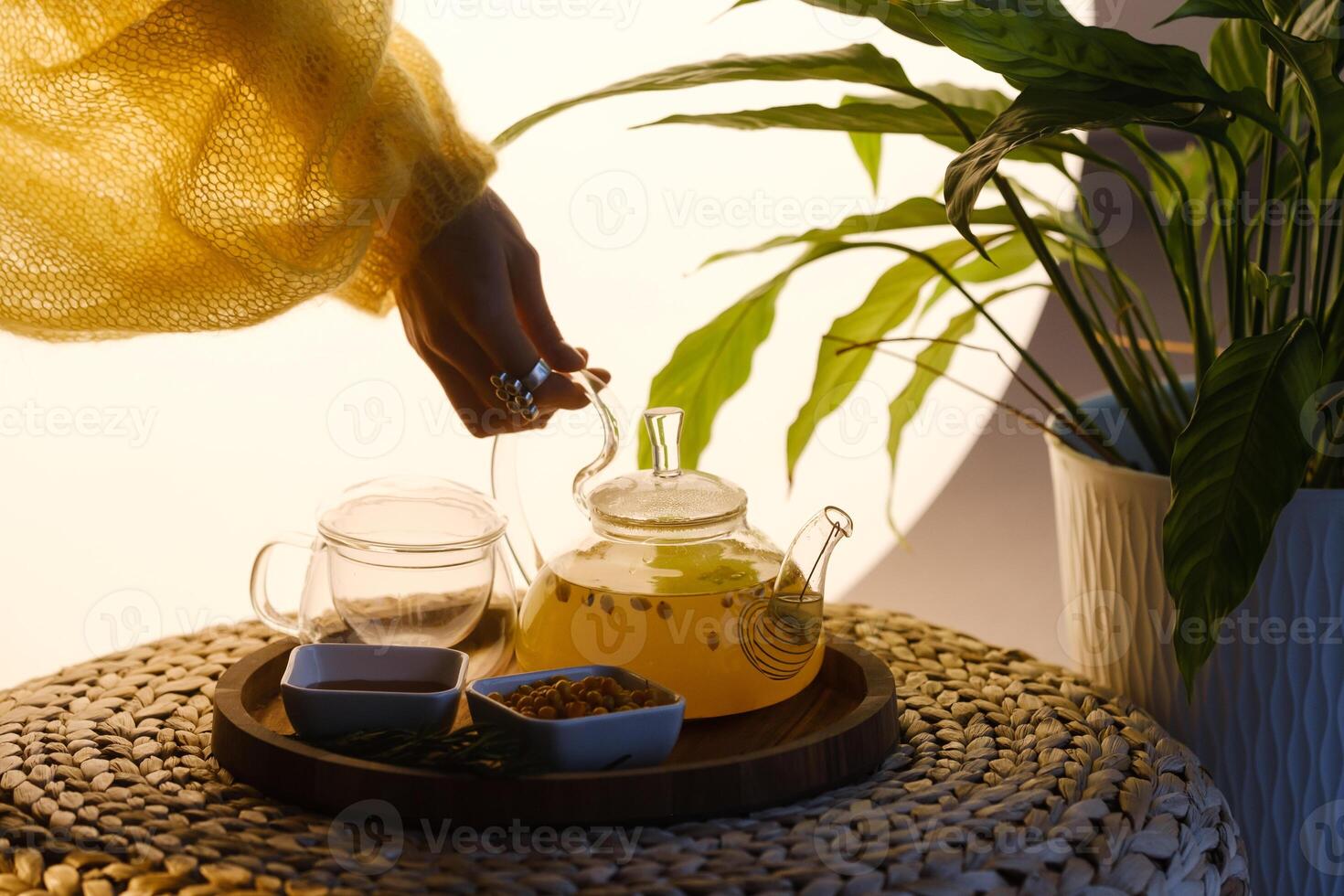 Close-up of a hand with a kettle. A teapot with sea buckthorn tea, honey and a plate with sea buckthorn on a tray photo